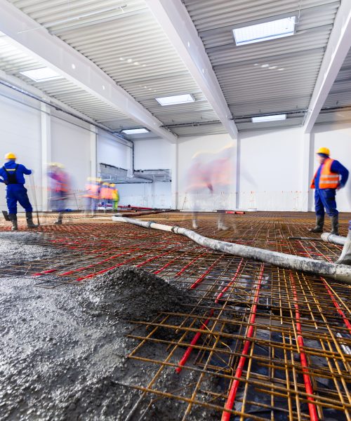 Workers do concrete screed on floor with heating in a new warehouse and office building. Interior finishing industry.